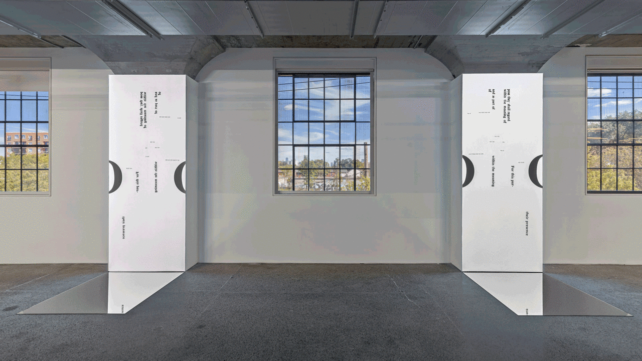 Three windows show outside of the museum's building and two pairs of two mirrors meet perpendicularly on the floor between the windows. The mirrors sitting against the wall show various text.