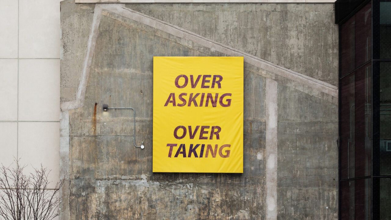 Large yellow print on building with the words "Over Asking Over Taking"